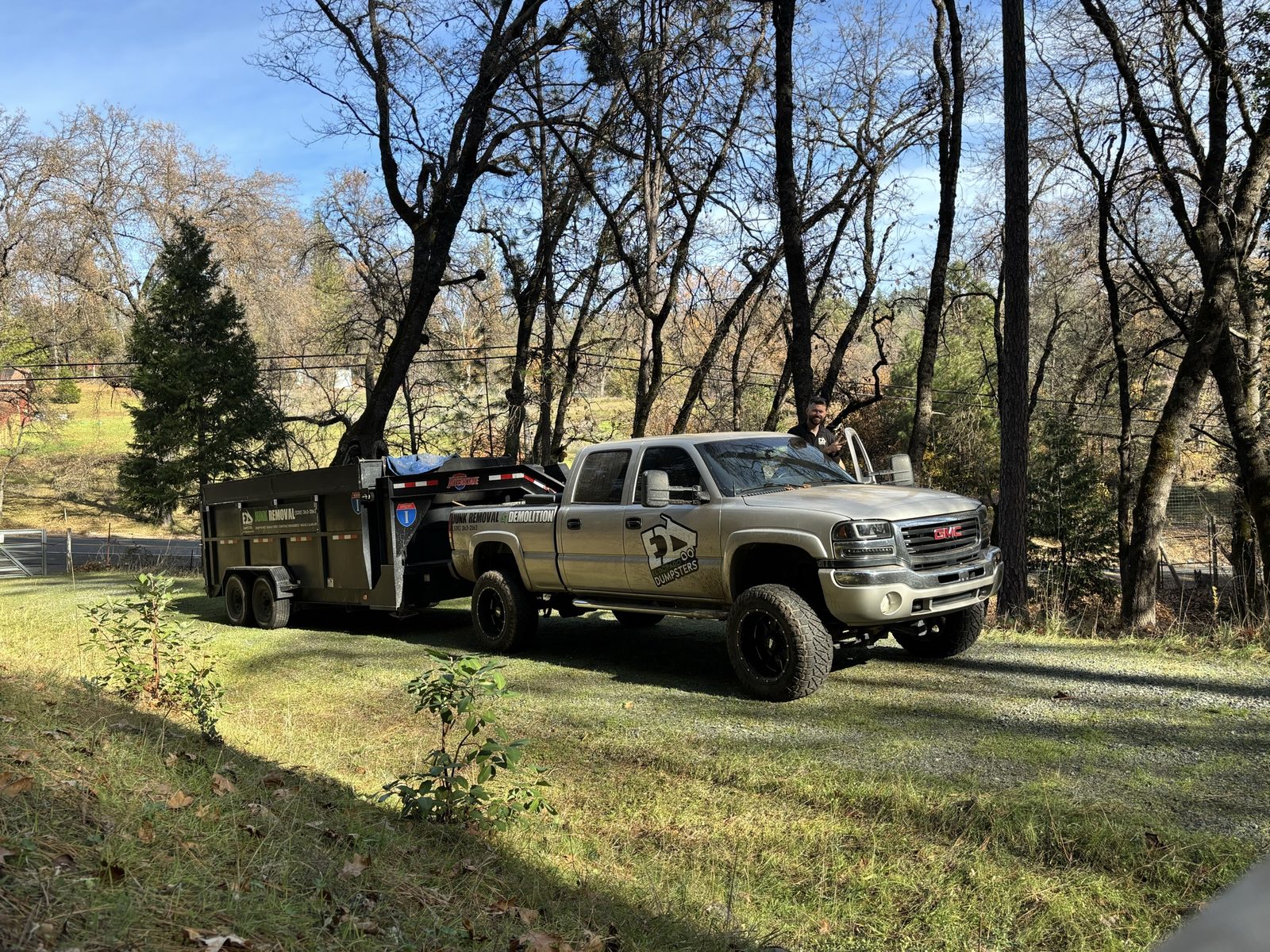 Branded El Dorado Dumpsters GMC truck and dump trailer on a wooded property